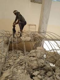 عامل يقوم بتكسير الخرسانة المسلحة باستخدام معدات الهدم في موقع بناء مع ارتداء معدات السلامة الكاملة لتنفيذ أعمال إزالة الخرسانة بدقة وأمان