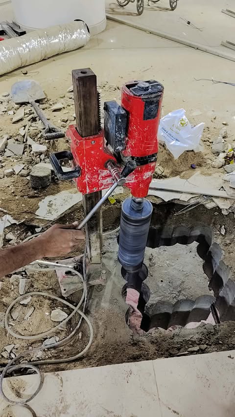 "مكينة كهربائية لتخريم الخرسانة، موضوعة على أرضية ورشة، تظهر أدوات القطع المعدنية ومقبض التشغيل"